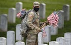 Wearing a face mask, a member of the 3rd U.S. Infantry Regiment also known as The Old Guard, places flags in front of each headstone for "Flags-In" at