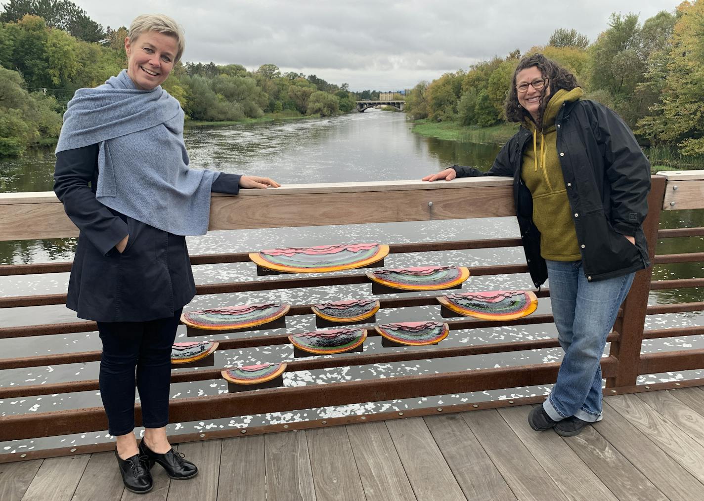 Public art, including this temporary sculpture of colorful fungi on a bridge spanning the Mississippi River, has been popping up around Grand Rapids this year, thanks to the city's Arts and Culture Commission. At left is Sonja Merrild, commission chair, with artist Nicole Camene.