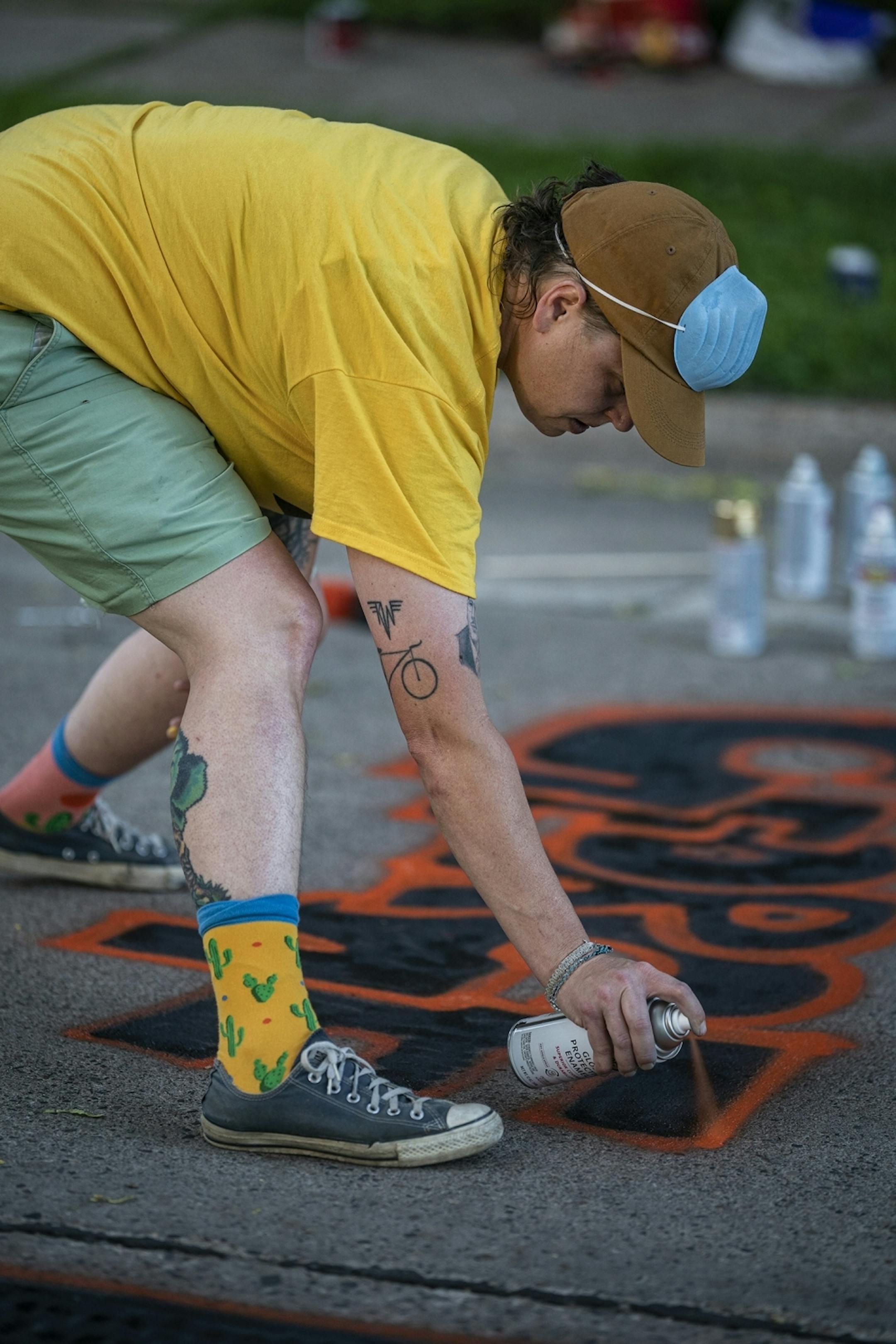 Teacher Cayla Baumann helps paint George floyd's name on top of a peace sign.