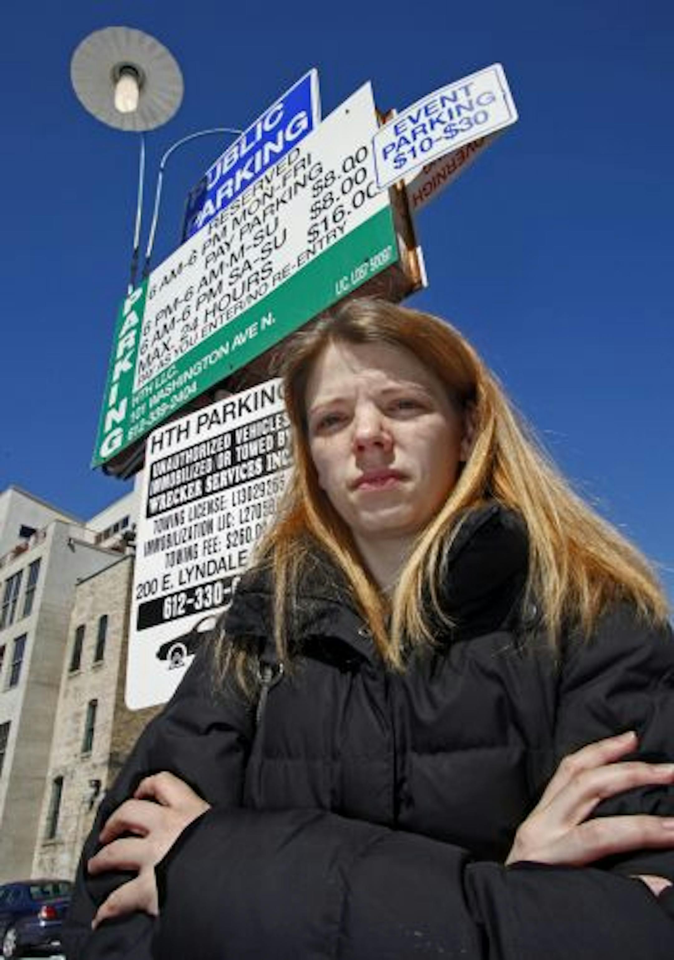 Nikki Daly in front of signs at the entrance to the parking lot adjacent to Runyon's where her car was towed.