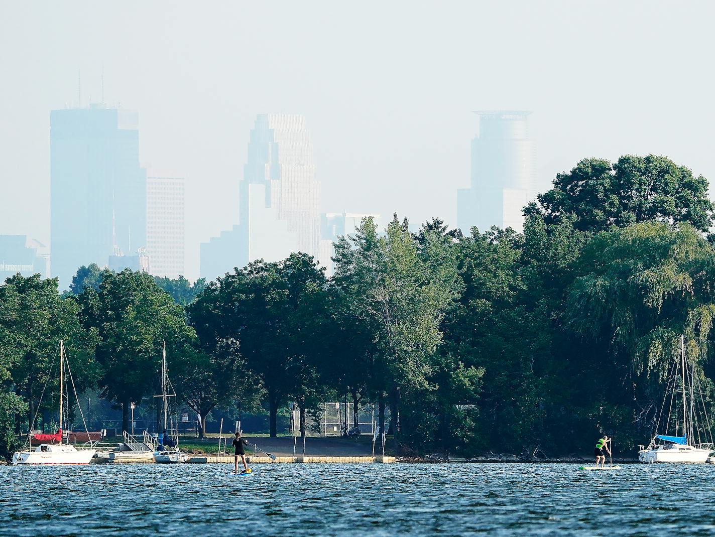 Haze from wild fires burning in Canada obscured the Minneapolis skyline as water boarders paddled along Lake Nokomis Thursday in Minneapolis. ]