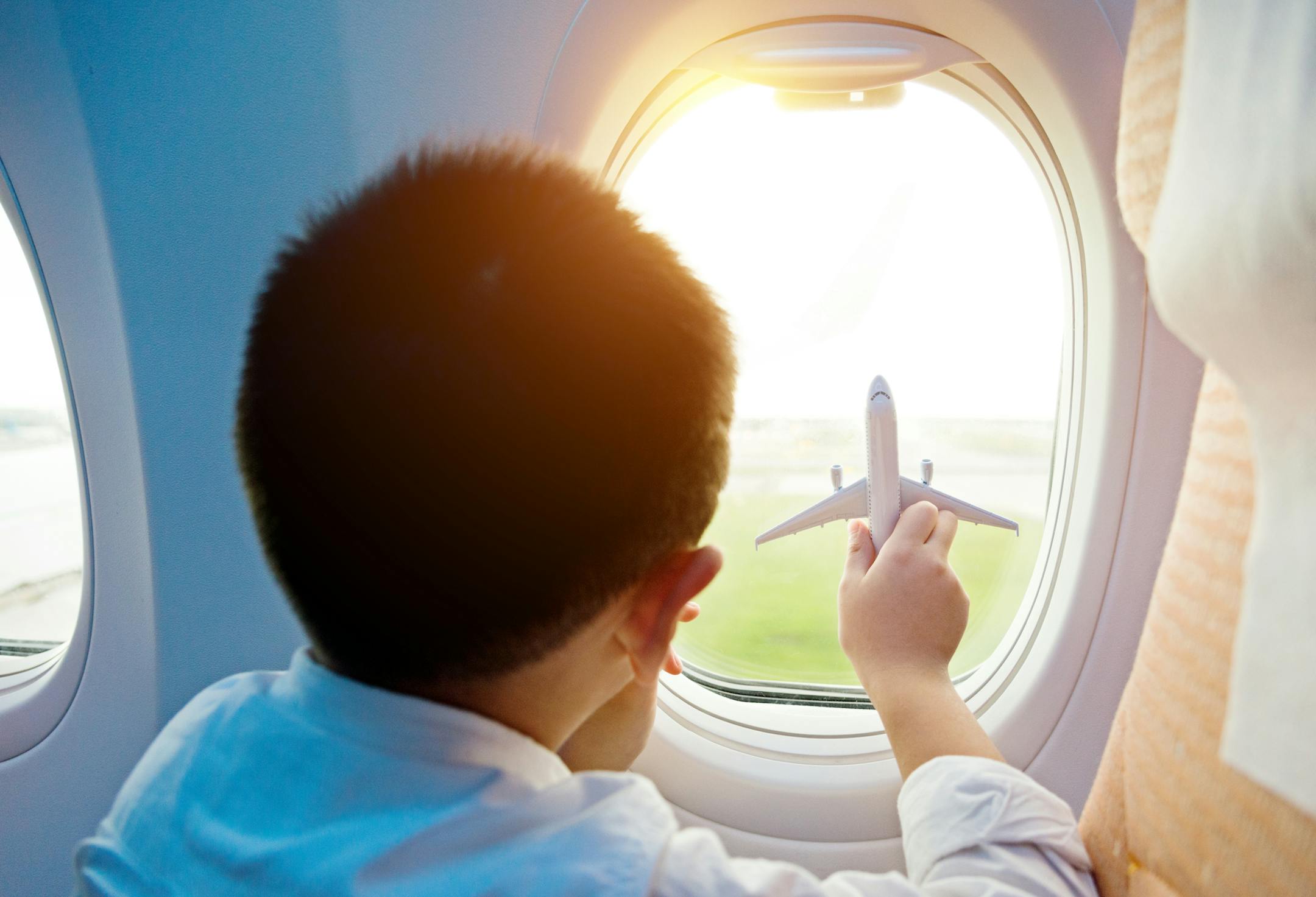 Little boy holding a toy plane and looking out of airplane window