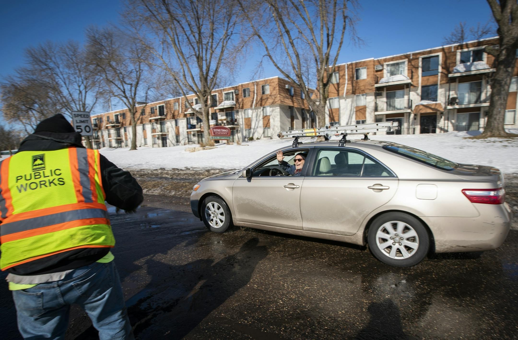 A driver waves and yells "thank you" while driving by St. Paul Public Works street service workers patching potholes on Shepard Road.