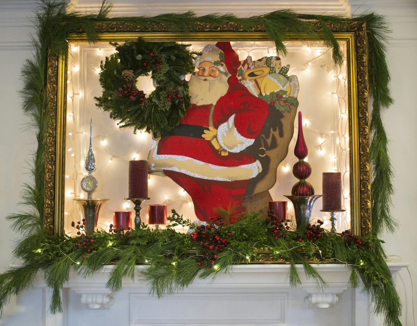 Designer Marsha Hunt created a shadowbox effect with festive white twinkle lights, a vintage gold frame and a wooden Santa Claus. The mantel is decorated with fresh greens accented with berries and multiple-height candles and ornaments.