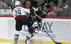 Colorado Avalanche's Nathan MacKinnon (29) pins Minnesota Wild's Jason Zucker (16) to the boards during the third period of an NHL hockey game Sunday,
