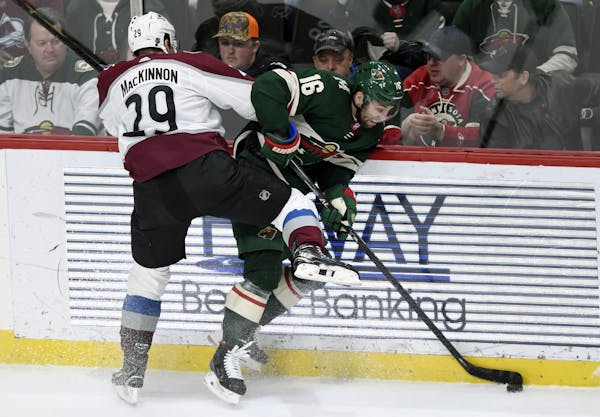 Colorado Avalanche's Nathan MacKinnon (29) pins Minnesota Wild's Jason Zucker (16) to the boards during the third period of an NHL hockey game Sunday,