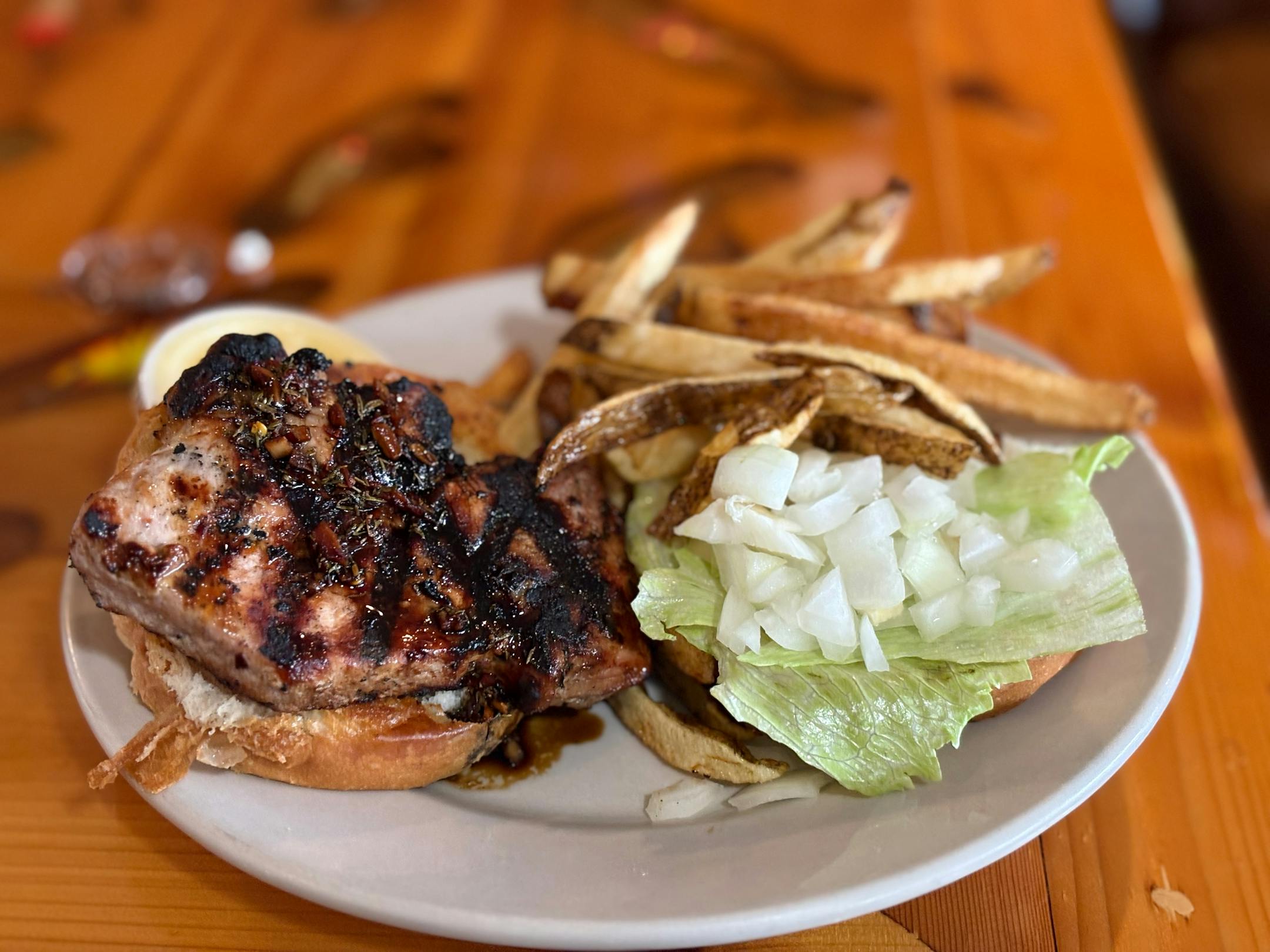 A grilled pork chop with jerk sauce on a bun with lettuce, onion and french fries.