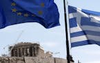A Greek and a European Union flag billow in the wind as the ruins of the fifth century BC Parthenon temple are seen in the background on the Acropolis