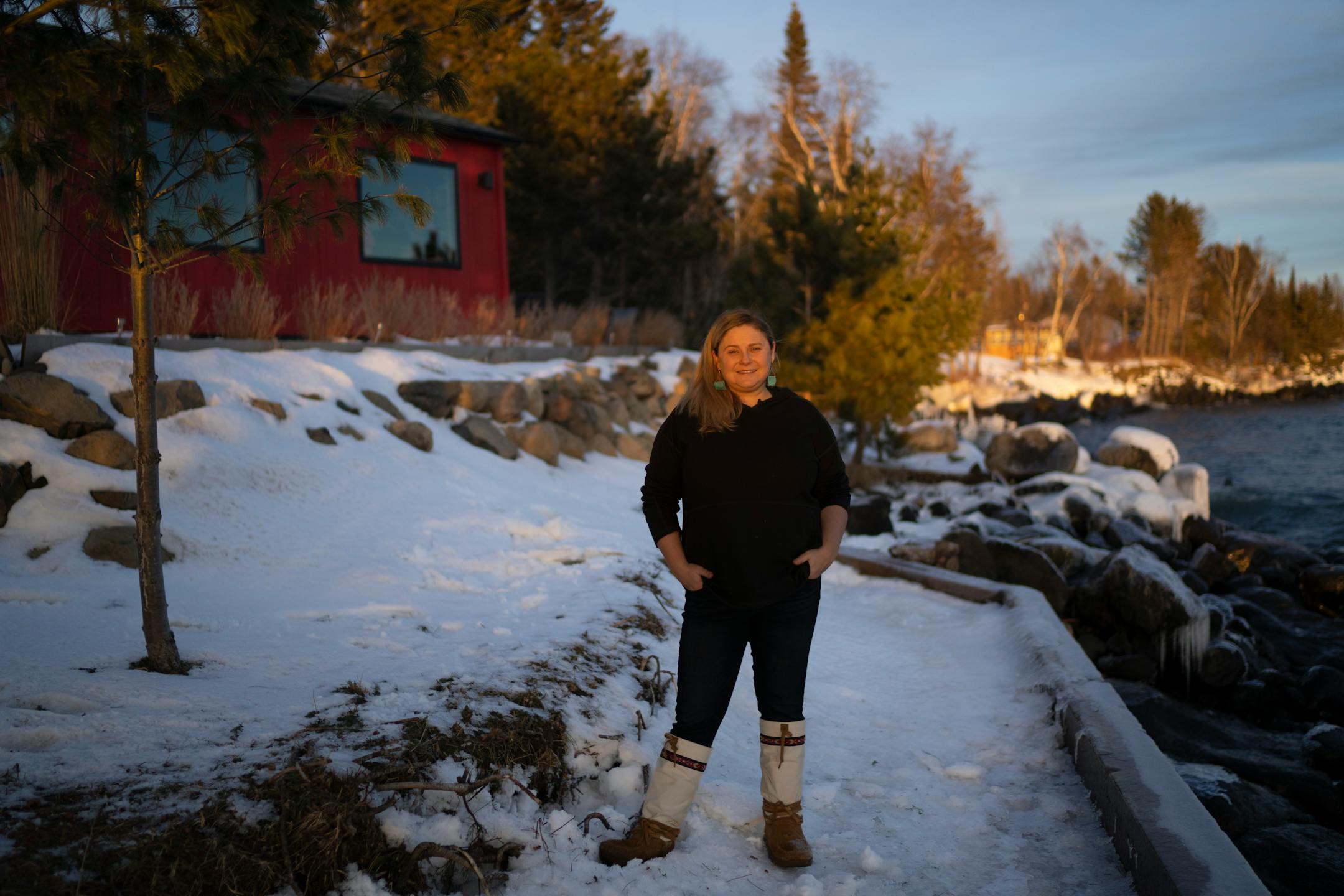Sisu and Löyly Sauna owner Katie Usem poses for a picture with the sauna behind her at left and Lake Superior at right in Grand Marais.