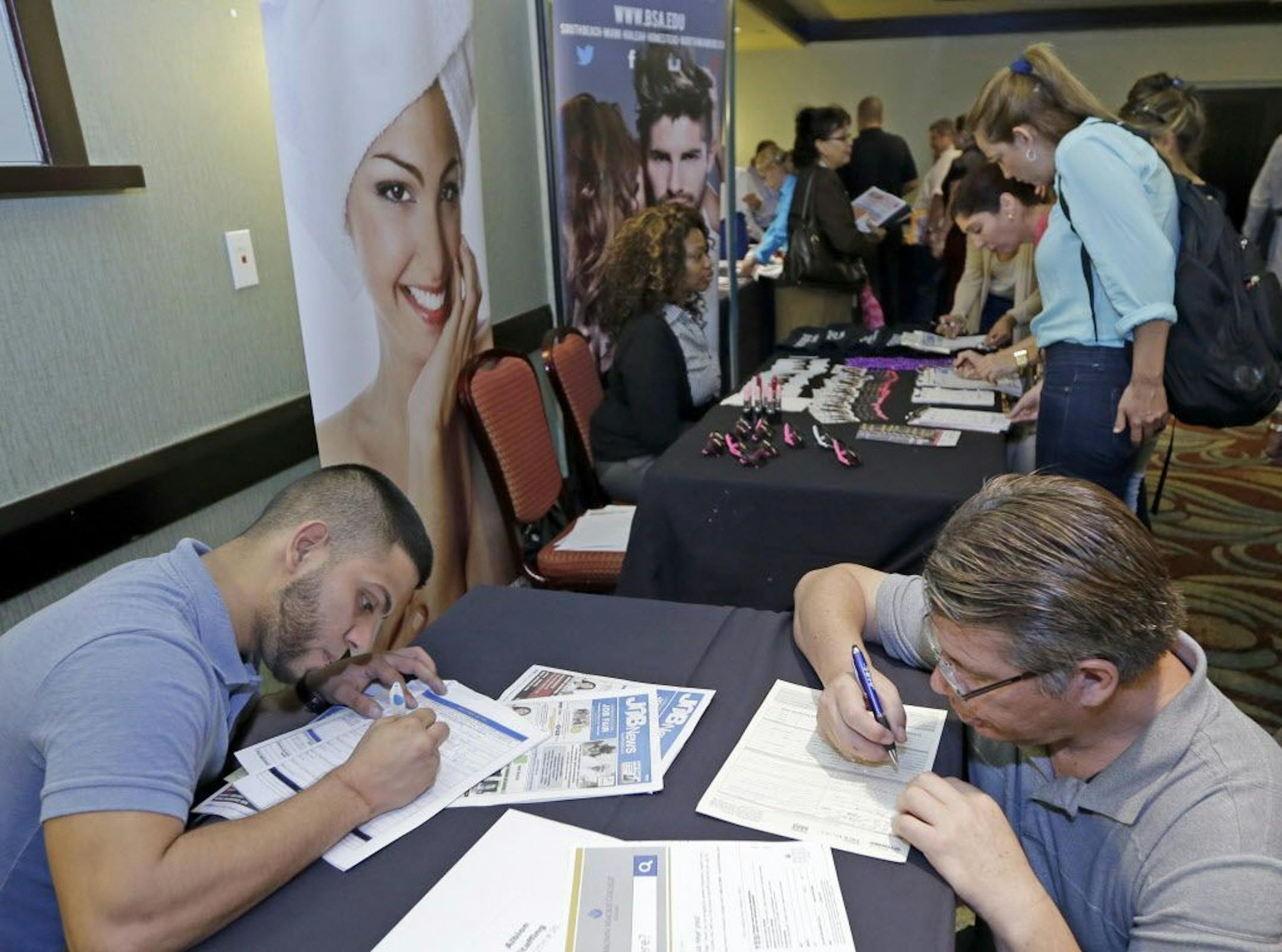 In this Wednesday, Oct. 22, 2014 photo, job seekers Stevens de la Pena, foreground left, and Eduardo Perez, foreground right, fill out a job application at a job fair in Miami Lakes, Fla. The Labor Department releases weekly jobless claims on Wednesday, Nov. 26, 2014.