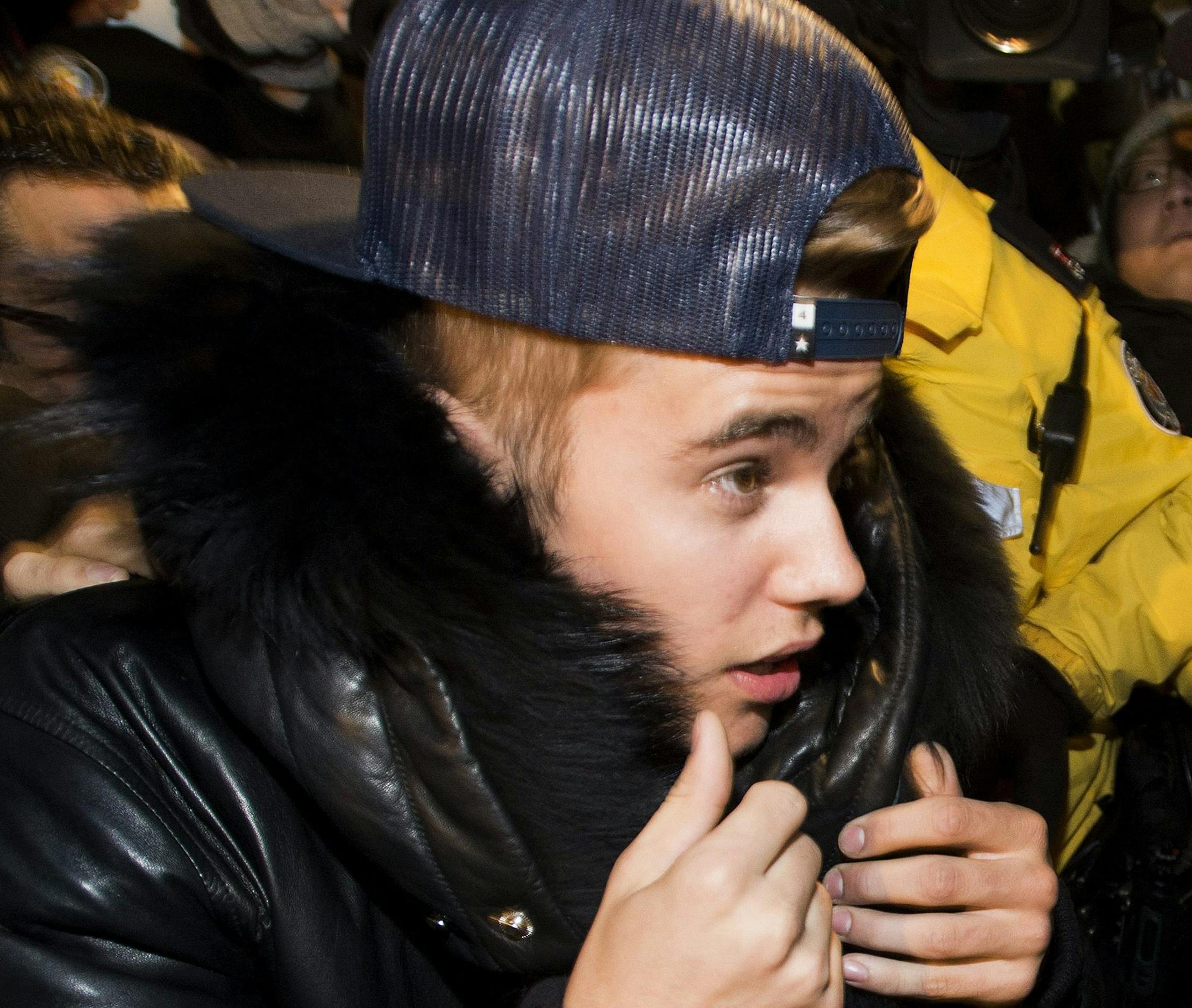 Canadian musician Justin Bieber is swarmed by media and police officers as he turns himself in to city police for an expected assault charge, in Toronto, on Wednesday, Jan. 29, 2014. A police official said the charge has to do with an alleged assault on a limo driver in December. (AP Photo/The Canadian Press, Nathan Denette