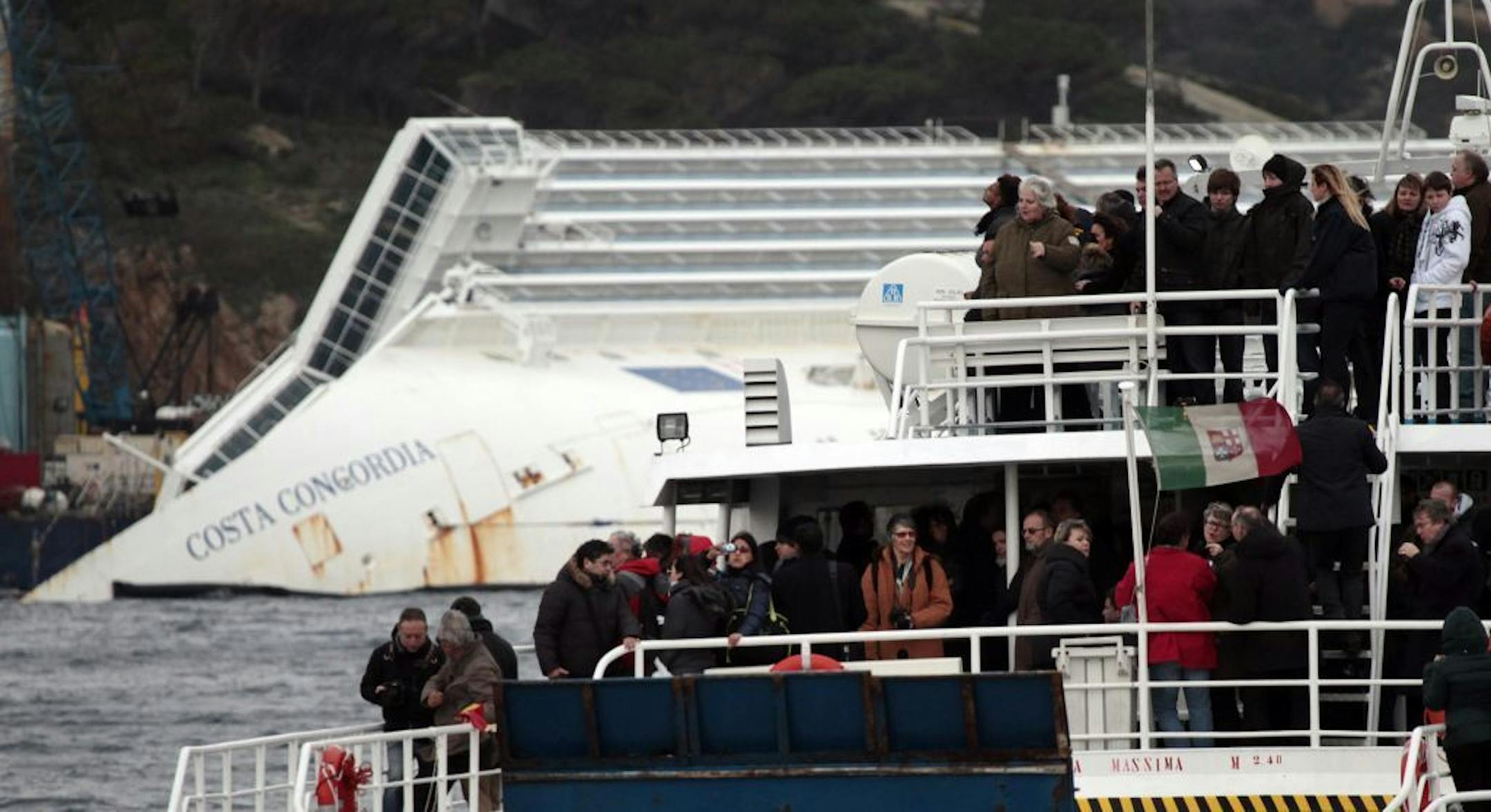 Relatives of the 32 victims of the Costa Concordia shipwreck, aboard a ferry approach the ship off the Tuscan Island Isola del Giglio, Italy, Sunday, Jan. 13, 2013. Survivors of the Costa Concordia shipwreck and relatives of the 32 people who died marked the first anniversary of the grounding Sunday. The first event of Sunday's daylong commemoration was the return to the sea of part of the massive rock that tore into the hull of the 112,000-ton ocean liner on Jan. 13, 2012 and remained embedded