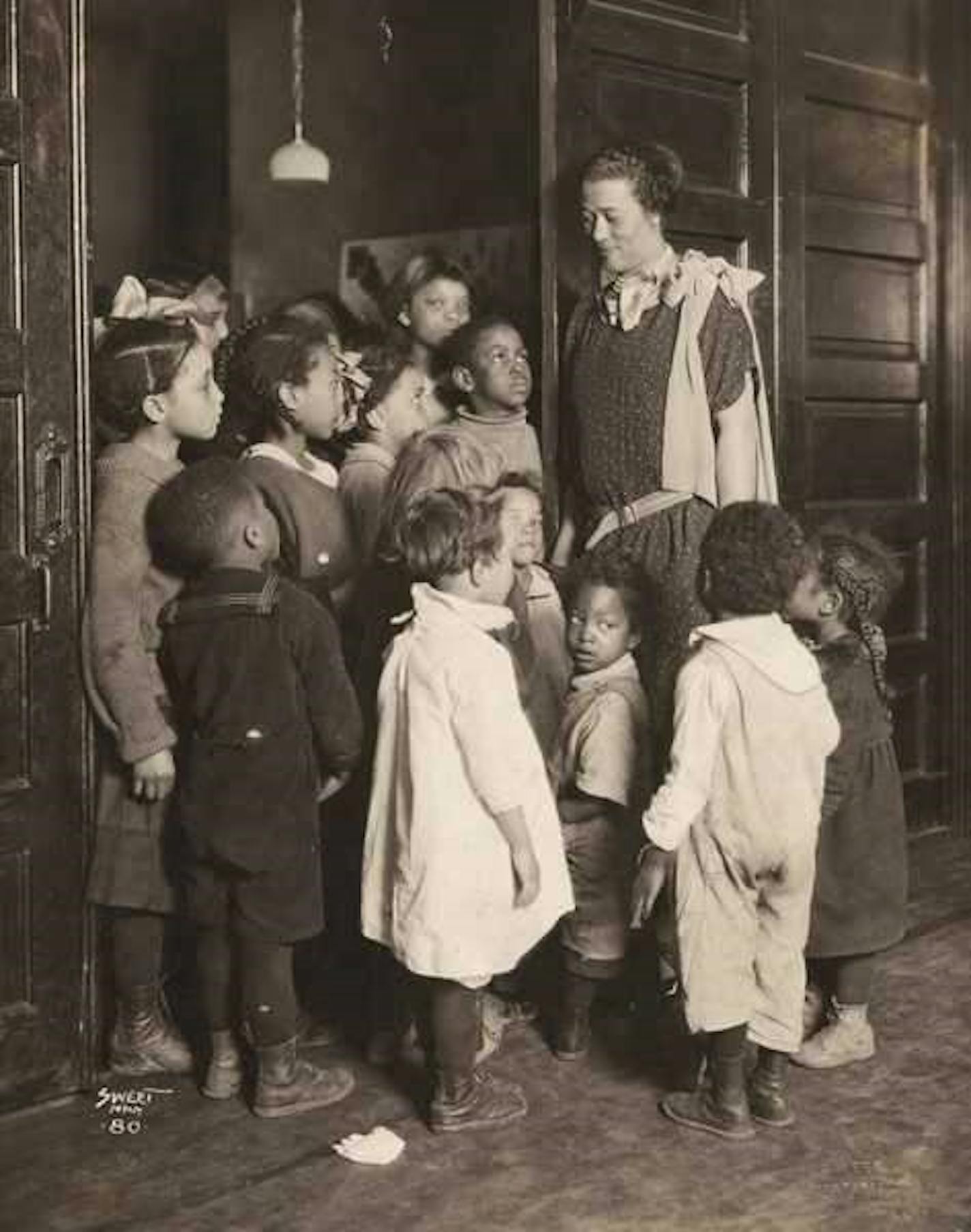 A group of kids of various ages stand around looking up at a woman.