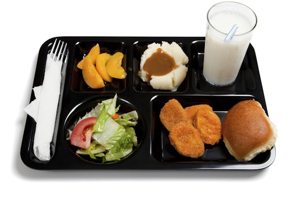 A black school lunch tray including tossed salad, chicken nuggets, roll, peaches, mashed potatoes and gravy with milk on a white background