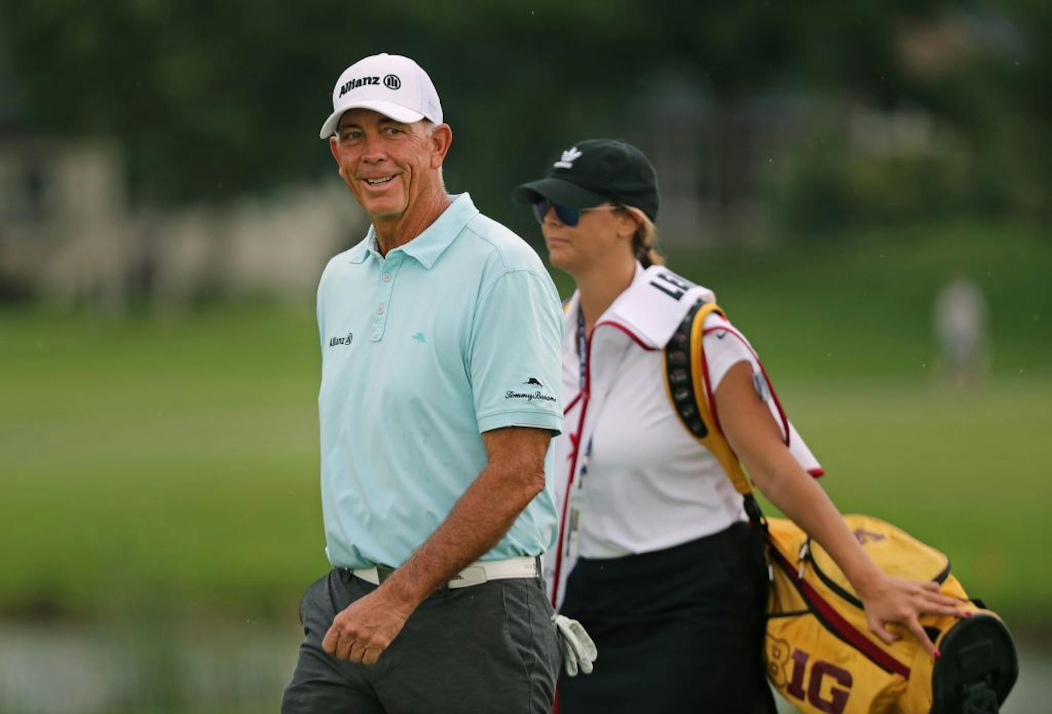 Tom Lehman smiled at cheering fans after teeing off at the first hole as his caddy carried his University of Minnesota golf bag behind him.