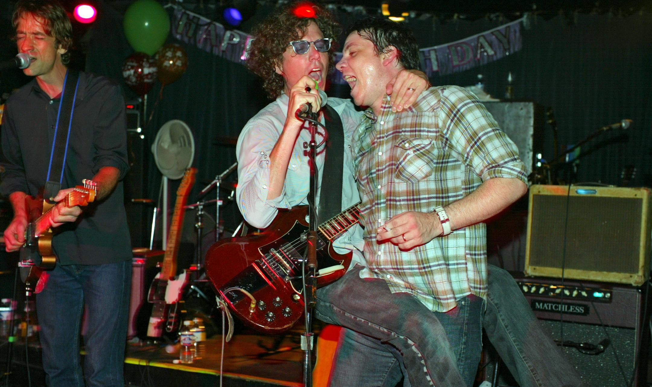 Gary Louris hopped got carried away, literally, by Jeff Tweedy as they sang backing vocals while Jim Boquist, left, sang lead on a Golden Smog number. GENERAL INFORMATION: MINNEAPOLIS - 8/7/03 - Golden Smog, the all-star, alt-country band featuring Wilco's Jeff Tweedy, Jayhawks' Gary Louris and Marc Pearlman, Soul Asylum's Dan Murphy, Iffy's Kraig Johnson and assorted others played a rare concert at the 400 Bar in Minneapolis Thursday night. ORG XMIT: MIN2014020417263057 ORG XMIT: MIN14020417382
