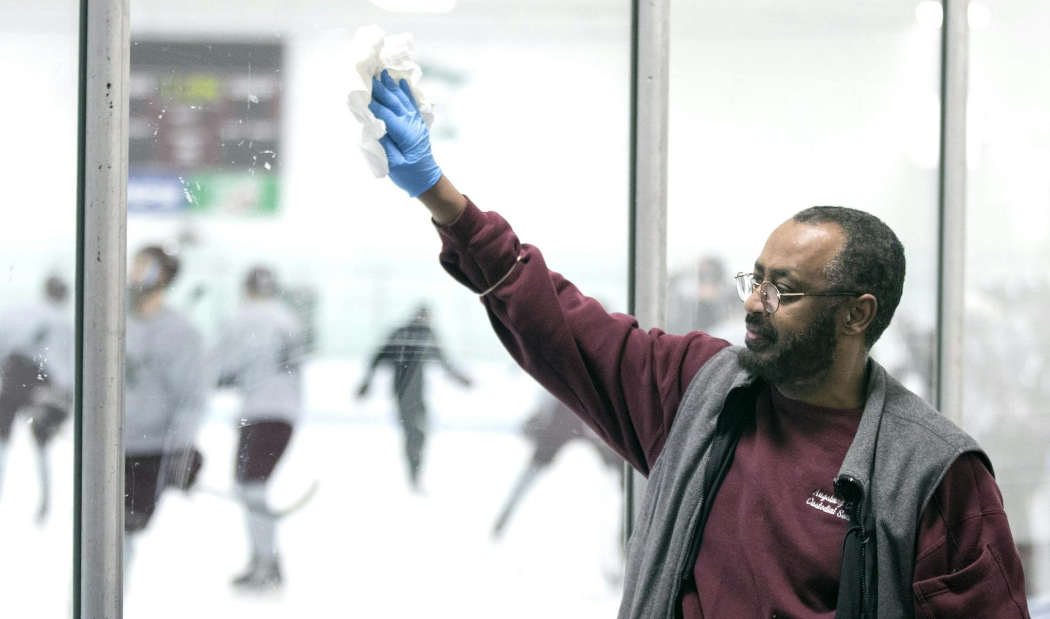 Minasie Theophilos a custodian for 25 years at Augsburg cleaned the glass at the rink during practice. After practice the team presented him with a 5,000 check to help him visit his home country of Ethiopia after 35 years away from his country Tuesday March 15, 2017 in Minneapolis, MN.] The Augsburg hockey team and others members of the school established a fundraiser for Minasie and raised the money within 24 hours. JERRY HOLT ï jerry.holt@startribune.com