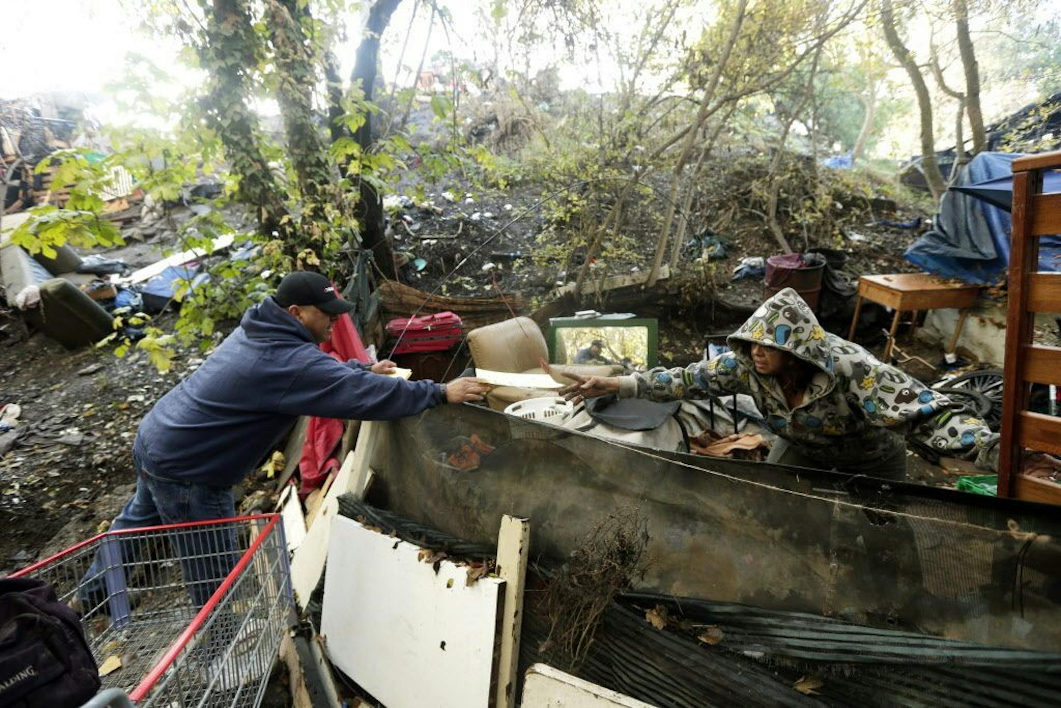 Carlos Tovar, a contractor in charge of cleanup, left, hands out a warning notice to a resident of the Silicon Valley homeless encampment known as The Jungle, Monday, Dec. 1, 2014, in San Jose, Calif.