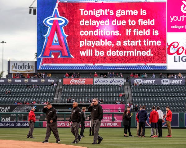 Umpire crew chief Gary Cederstrom conducted a phone conversation as the Angel Stadium grounds crew used tarps, squeegees, small pumps and aeration mac