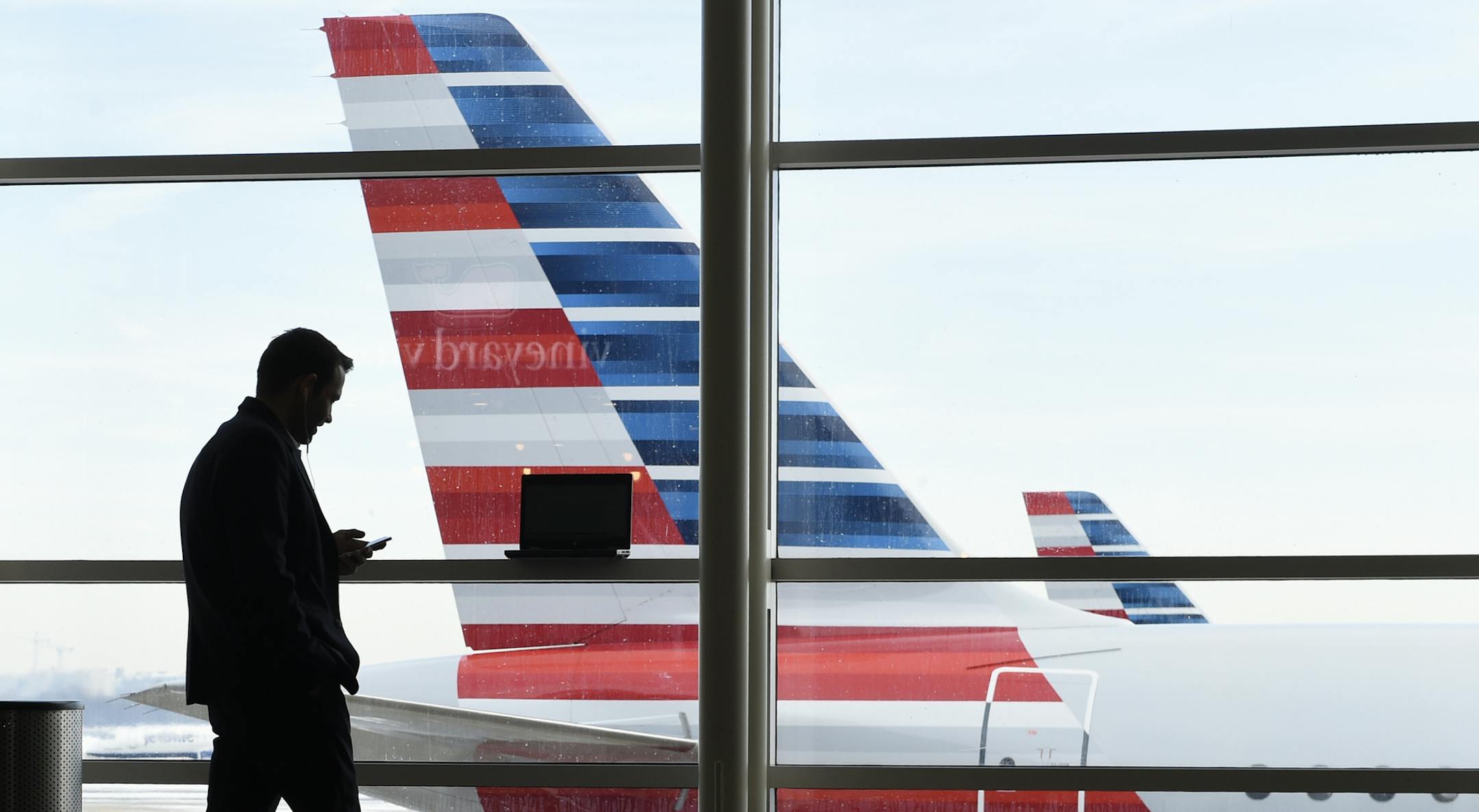 FILE - In this Jan. 25, 2016, file photo, a passenger talks on the phone as American Airlines jets sit parked at their gates at Washington's Ronald Reagan National Airport. American Airlines announced Wednesday, Jan. 18, 2017, that passengers will be able to buy ìbasic economyî tickets starting in February that will be similar to bare-bones fares already offered by Delta Air Lines and soon to be matched by United Airlines. The basic-economy fares will have a lower price, but will offer