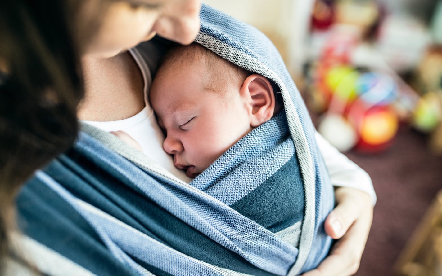 Close up of unrecognizable young mother with her newborn baby son in sling at home