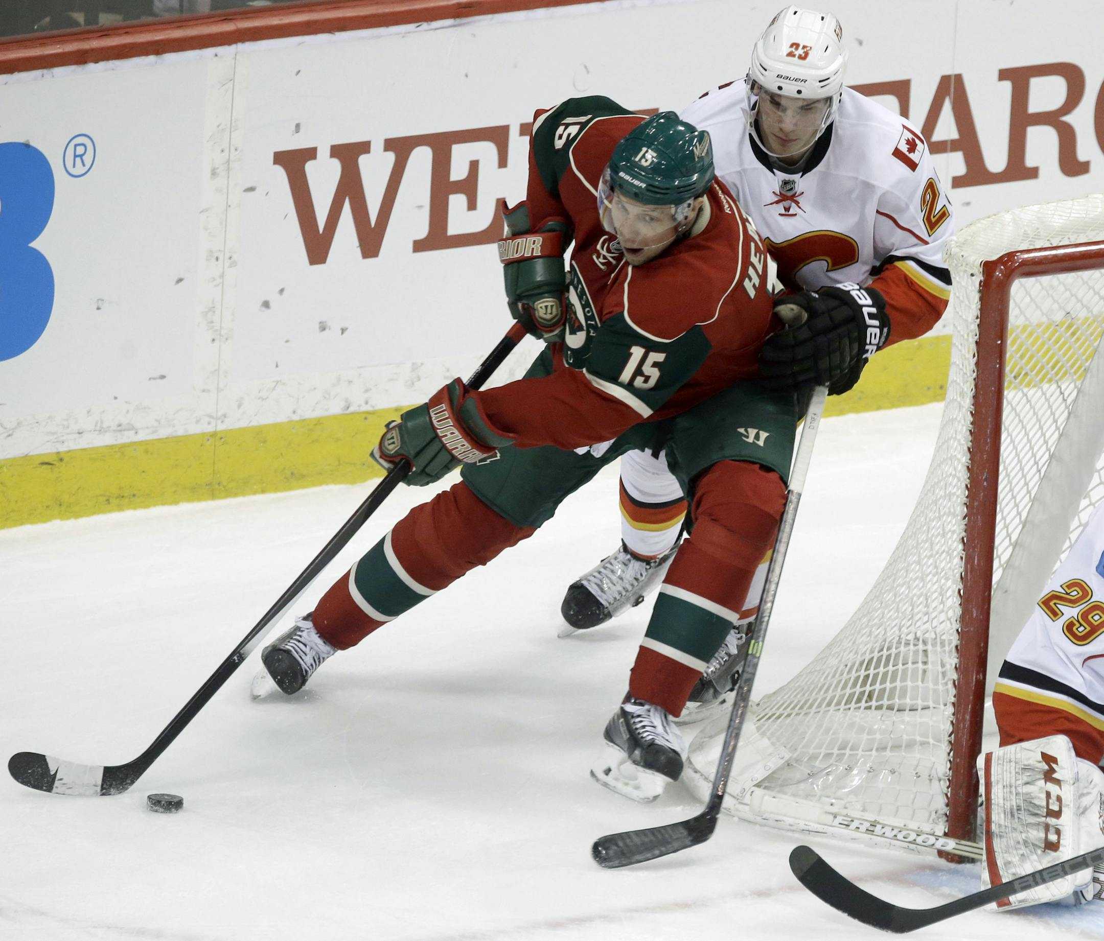 Minnesota Wild's Dany Heatley, left, cuts the corner as he is pursued by Calgary Flames' Sean Monahan as goalie Reto Berra, right, defends the net in the first period of an NHL hockey game, Monday, March 3, 2014, in St. Paul, Minn. (AP Photo/Jim Mone)