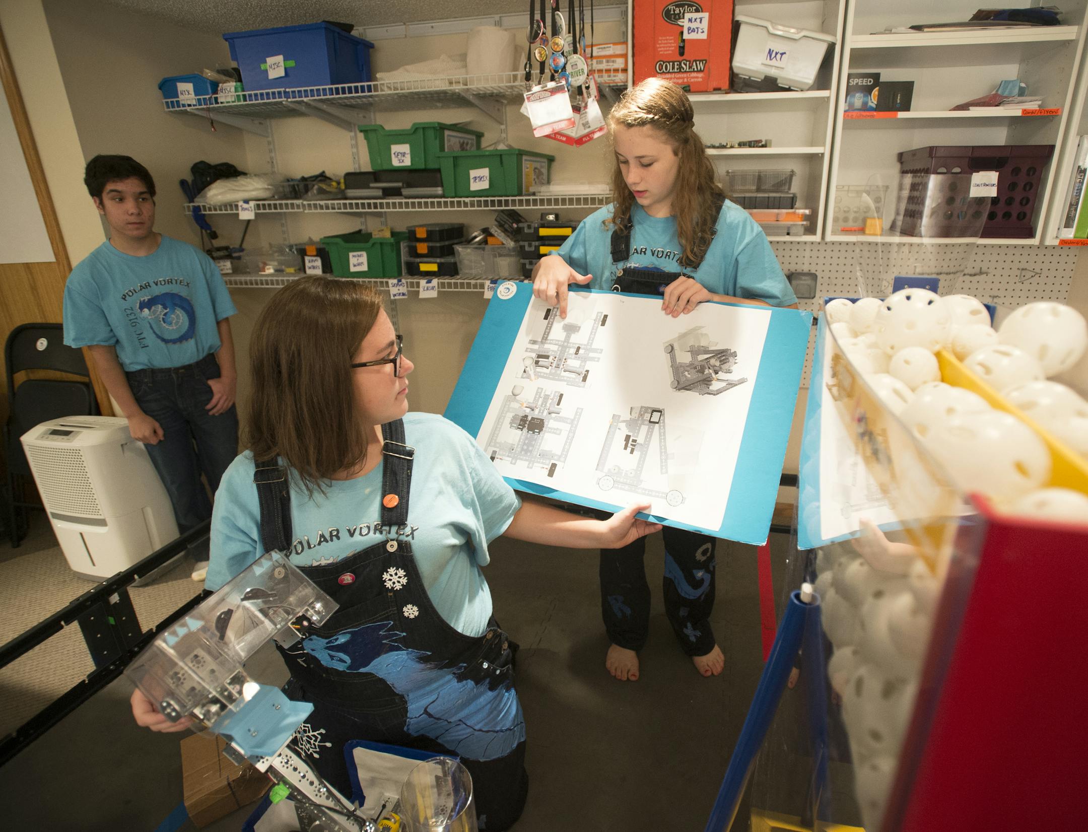 High school freshmen Bella Vandenbos, left of center, and Corrie Hester held up the blueprints for their robot, &#x201c;FrostByte,&#x201d; during a meeting of the Polar Vortex robotics team in Hester&#x2019;s basement Tuesday night.
