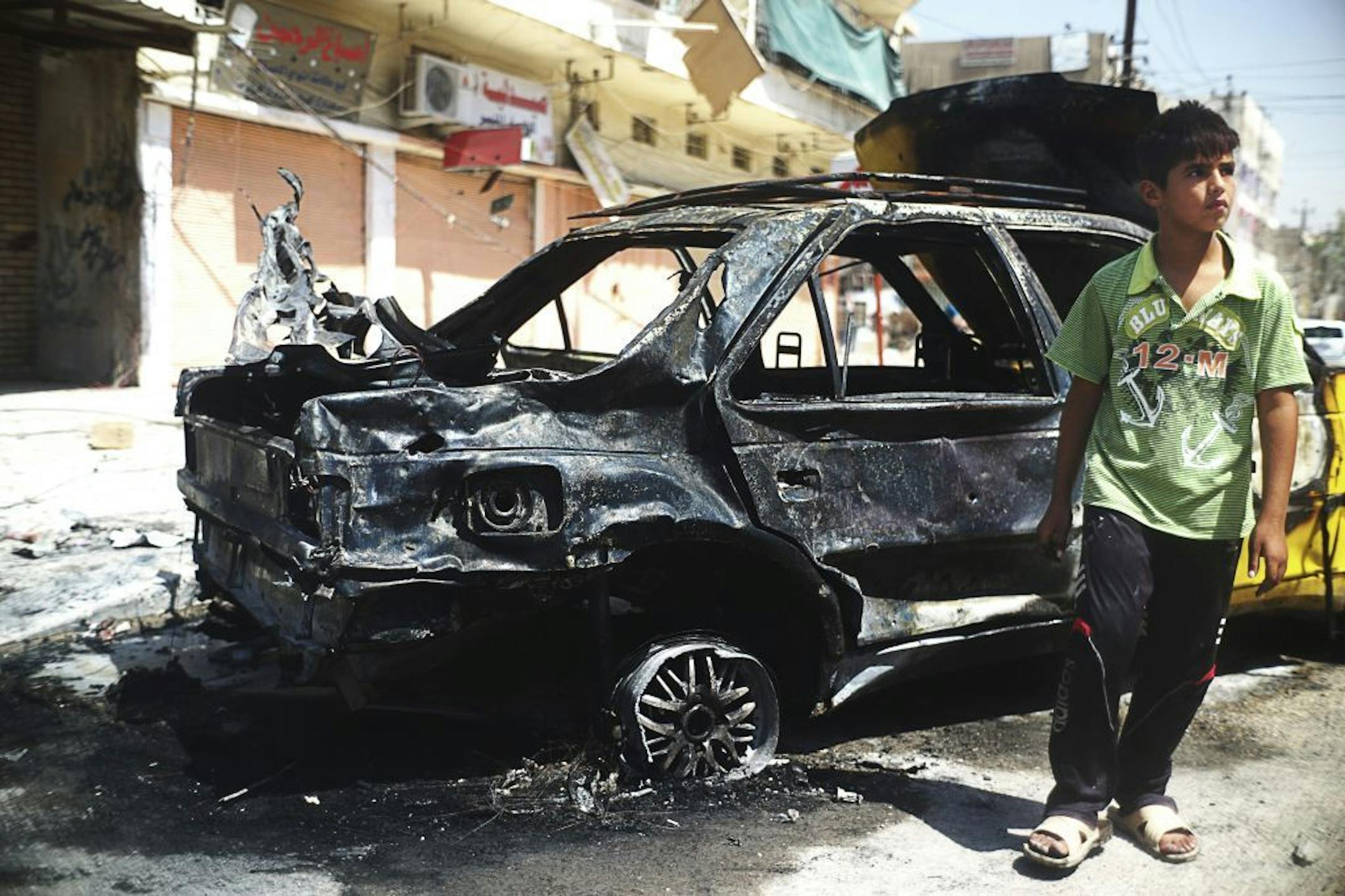 A boy passes the wreckage of a car following a car bomb explosion in Baghdad, Aug. 28, 2013. In the span of roughly an hour, on Wednesday, more than a dozen explosions struck around the city, killing at least 65 people and wounding far more, in the latest series of terrorist attacks that have engulfed Iraq.