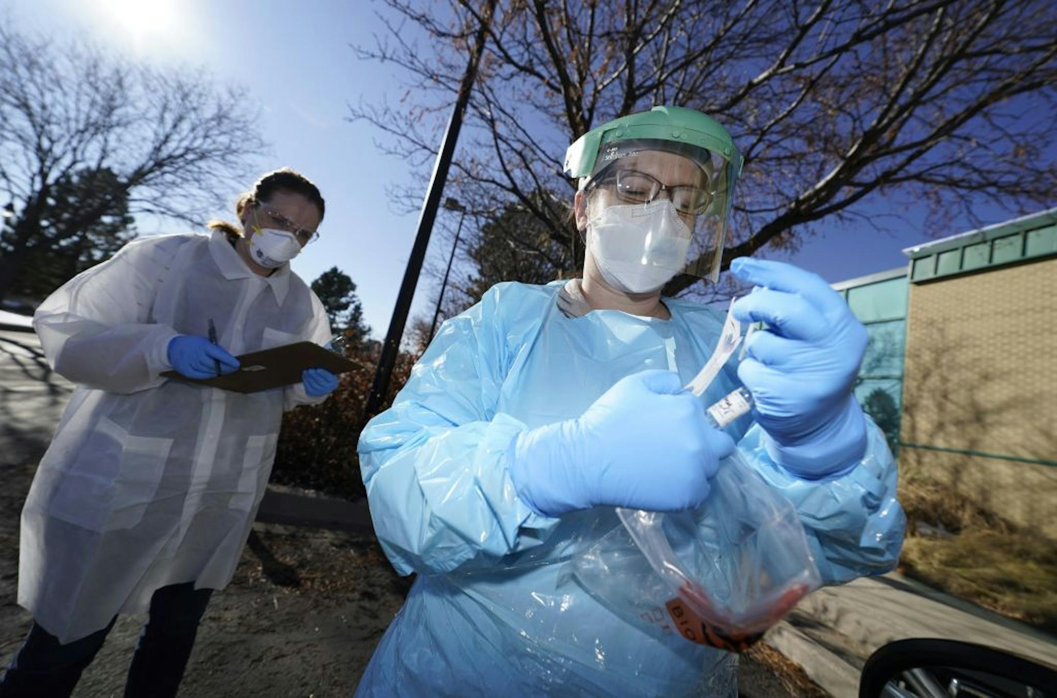Emily Travanty, back left,, laboratory director for the Colorado Department of Public Health and Environment, writes information as Sarah Totten, director of the department's microbiology program, places a swab in a bag after performing a nasal test for coronavirus for a patient Friday, Nov. 27, 2020, in east Denver.