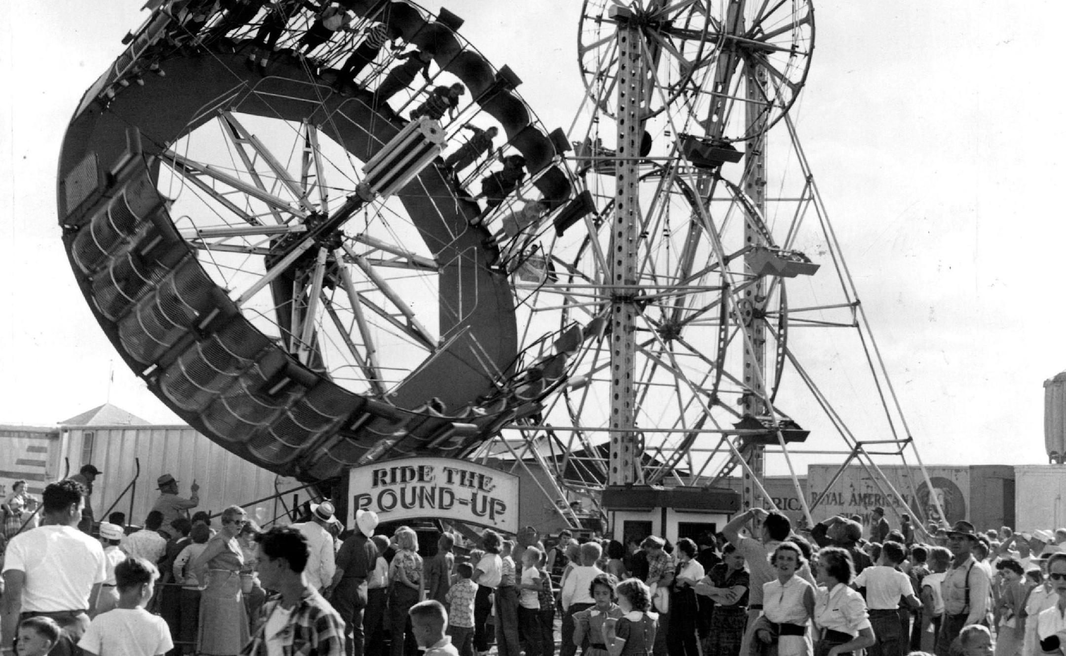 August 21, 1955 The "flying saucer" objects in the night view (above) turn out to be two midway rides by day (left). They happen to be two of the most popular rides the Royal American Shows will bring to the 1955 Minnesota State fair. At the left, in each photo, is "The Roundup." Customers are strapped in niches around its circular side, then whirled around while the plat-form is tilted to near-vertical position. The other ride, called "Giant Sky Wheels," is really two Ferris wheels revolving on