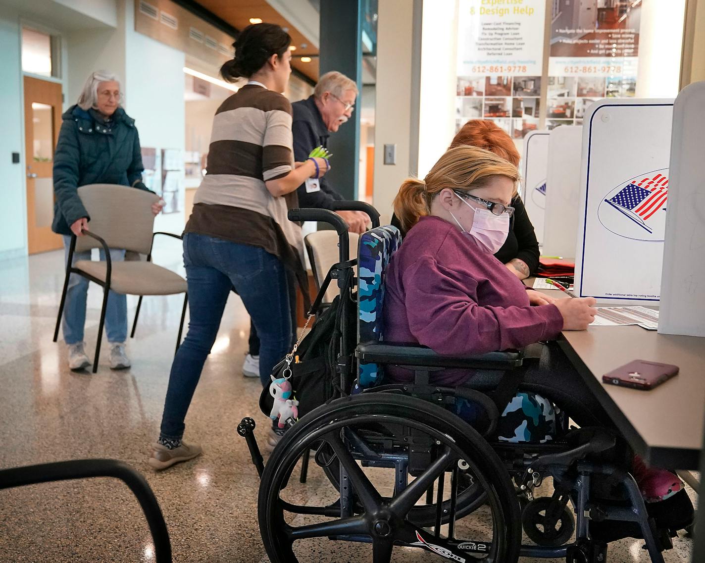 Raven Moe, 26, who has spina bifada, a spinal condition that has left her paralyzed from the waist down and in a wheelchair, fills out a ballot at the Richfield administrative offices while seated next to her mother Judy Moe (not pictured) Monday, Oct. 24, 2022 in Richfield, Minn. The mother and daughter have been at the forefront of a growing movement to expand access to voting and amplify disability issues ahead of the midterm elections. ]