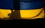 A man holding sunflowers casts a shadow on a Ukrainian flag during a rally held to show support for Ukraine in Los Angeles, Friday, March 11, 2022. (A