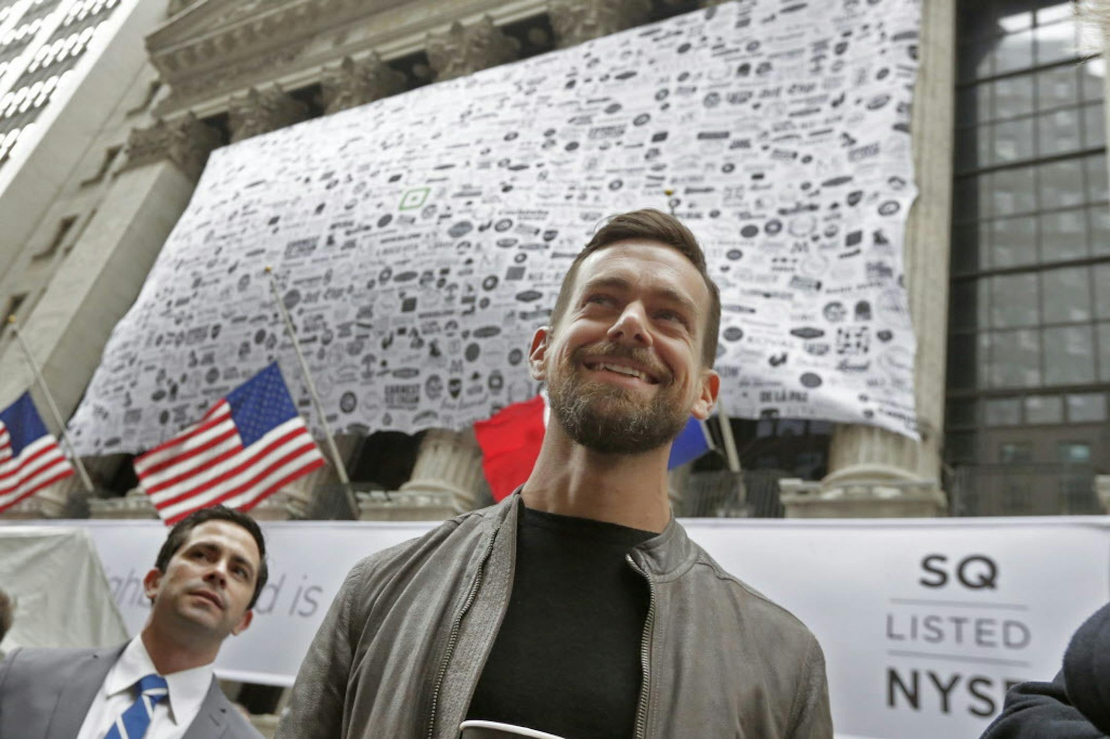 Square CEO Jack Dorsey, foreground, visits outside the New York Stock Exchange before opening bell ceremonies, Thursday, Nov. 19, 2015. Square, the 6-year-old startup known for its white, cube-shaped card readers that plug into smartphones, is surging in its first day as a publicly traded company. (AP Photo/Richard Drew)