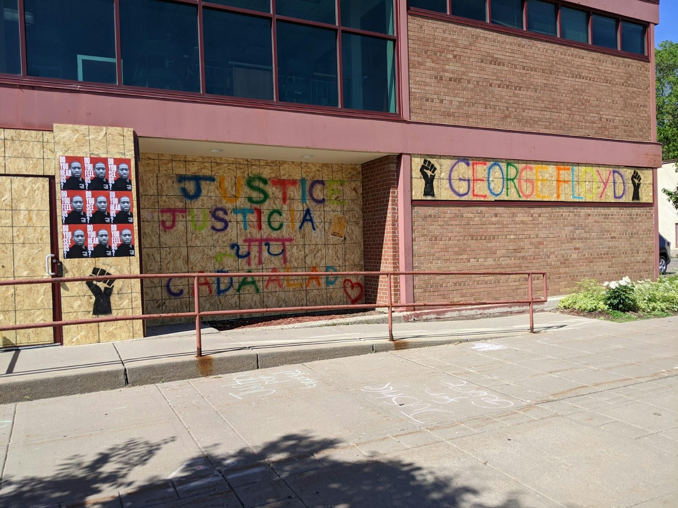 A series of black fists in the air and bilingual text calling for justice cover the boarded-up windows and doors at Capi Building, 3702 E Lake St.