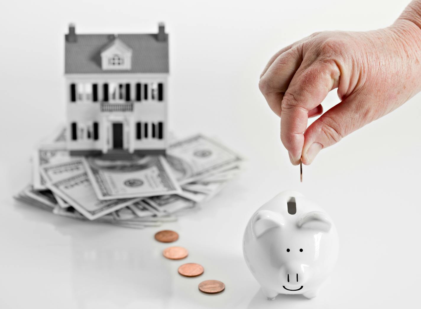 A conceptual image showing a reverse mortgage with a home sitting on a pile of money and a hand dropping coins slowly in a piggy bank. istock photo