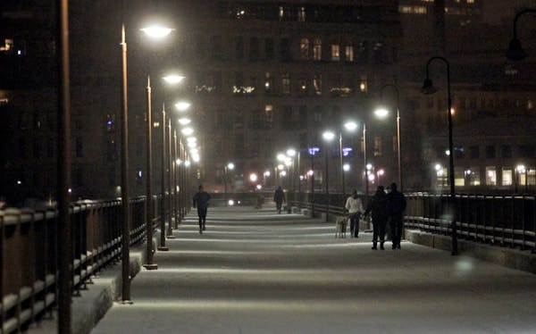 Pedestrians and a runner share the freshly blanketed Stone Arch Bridge during what may turn out to be the Twin Cities metro's first significant snowfa
