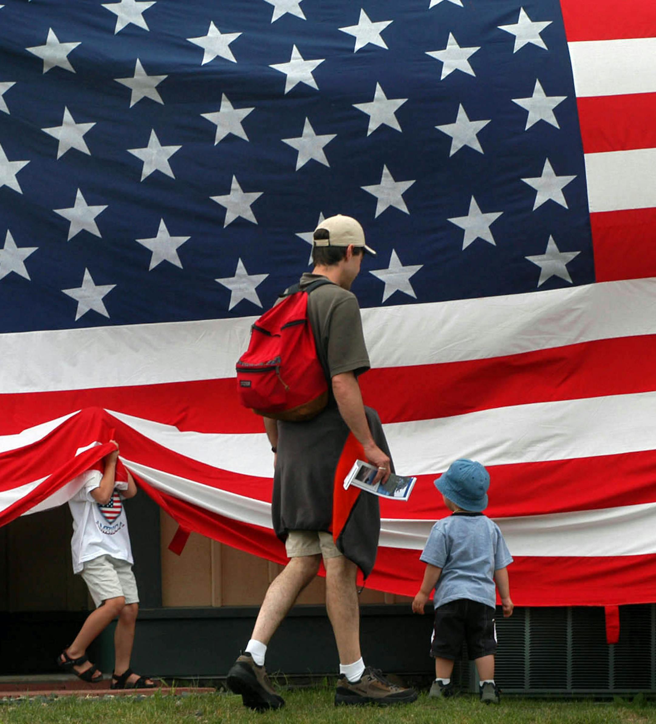 Richard Sennott/ Star Tribune Pequot Lakes, Mn Monday 7/4/2005 Fourth of July in Pequot Lakes In this Picture: from L to R Teddy Scheett 5yrs old of Brainerd and Tom Spizzo of Breezy Point with his 2 yr old son Aiden investigate a huge American flag fling in downtown Pequot lakes on the Fouth of July