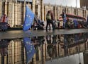 Protestors are reflected in a puddle as they wave European flags to demonstrate against Brexit in front of the Parliament in London, Monday, Dec. 3, 2