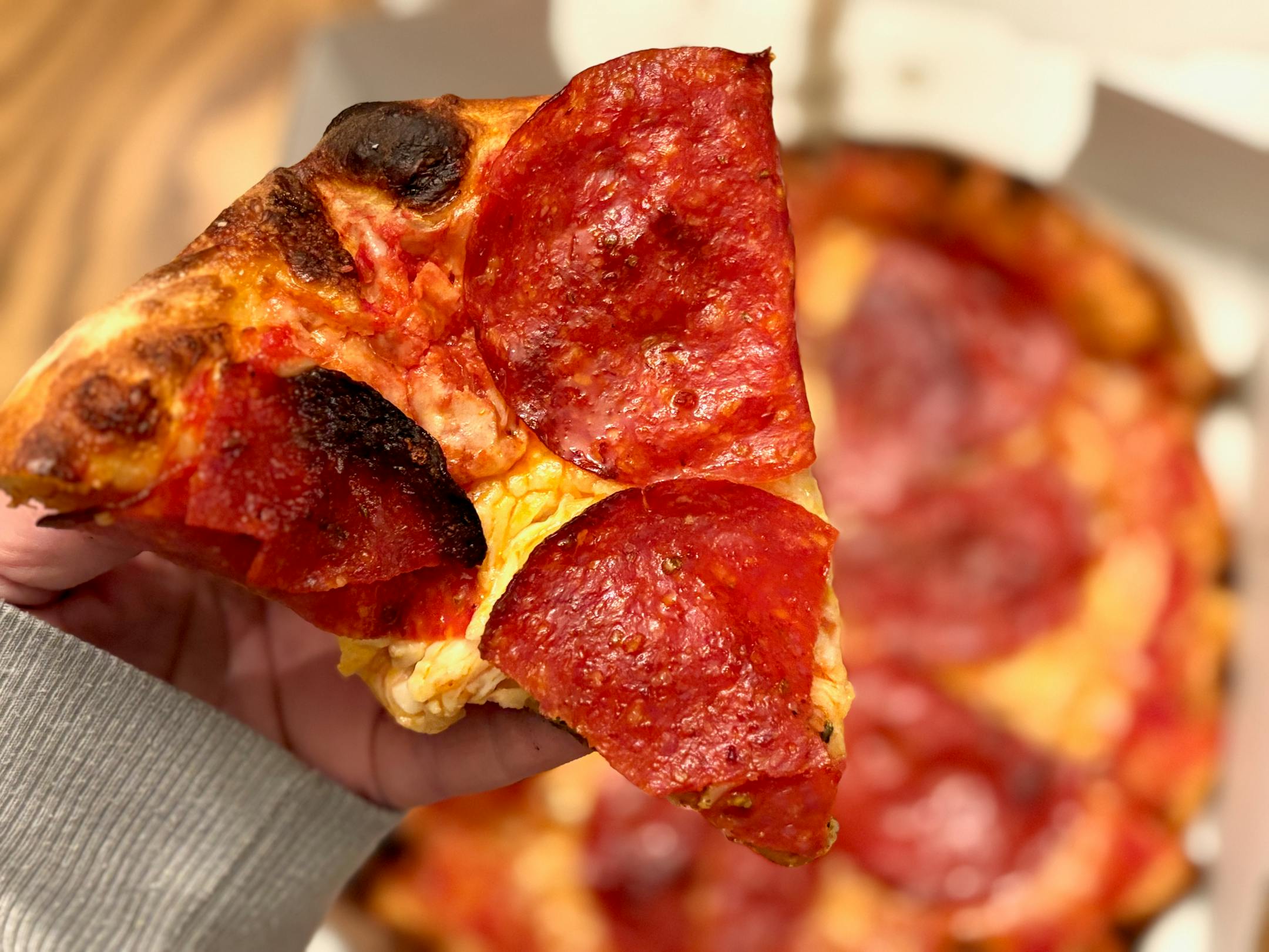 A slice of pepperoni pizza held over the rest of the woodfired pie.