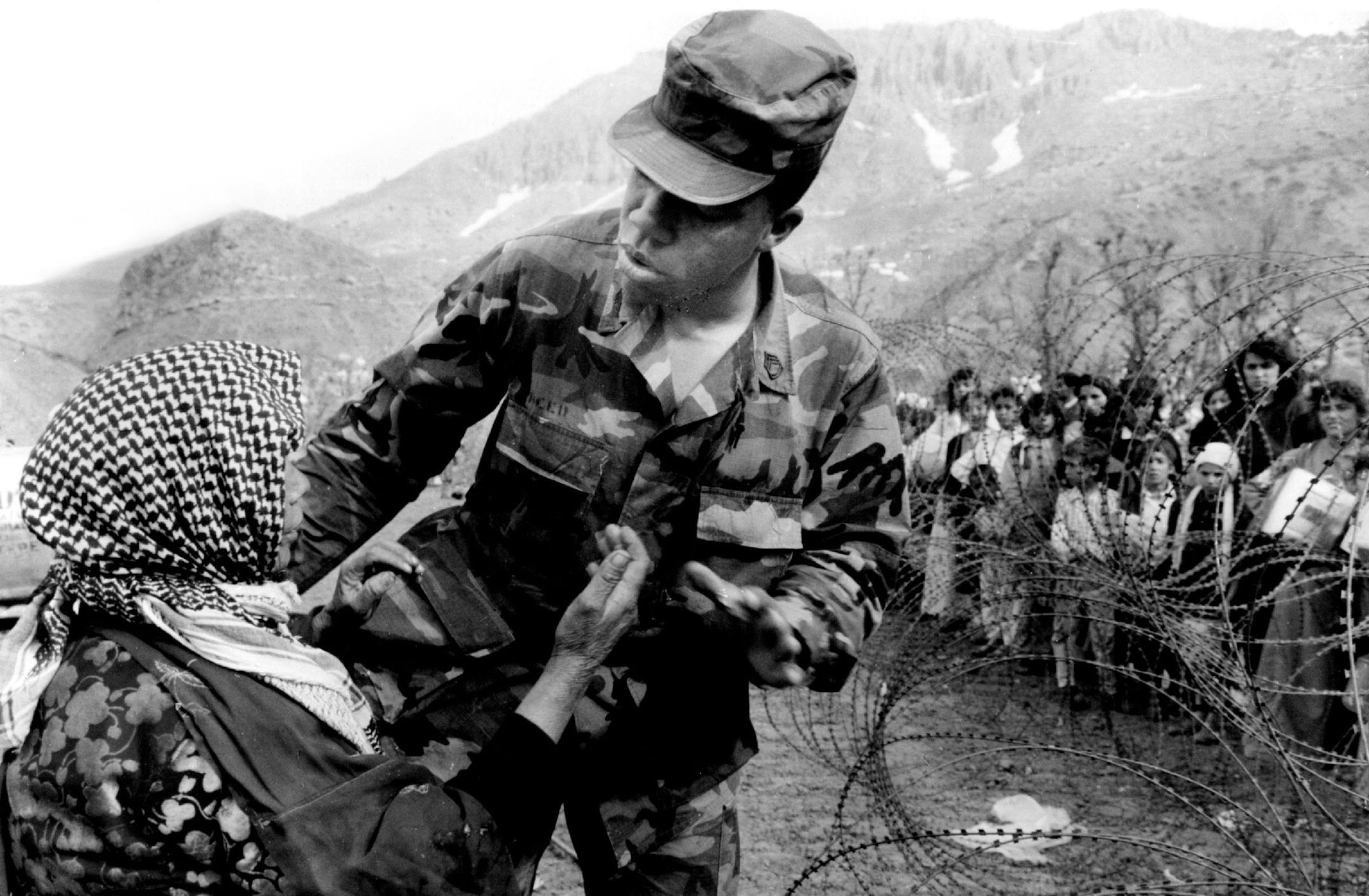 May 2, 1991 Background Info : Caption For This Pic : An elderly woman who had sneaked under a rope holding back scores of refuges in Isikveren camp waiting for water was escorted outside the barbed wire by as US soldier trying to keep some semblance of order to the distribution. May 6, 1991 Stormi Greener ORG XMIT: MIN2014081112542560