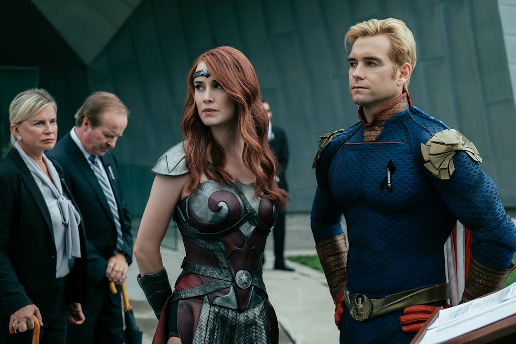 Homelander (Antony Starr, right) is the sociopathic Superman analog in “The Boys,” who has closeted lesbian Wonder Woman analog Queen Maeve (Dominique McElligott, center) under his thumb, along with the rest of The Seven, a thinly veiled Justice League.
