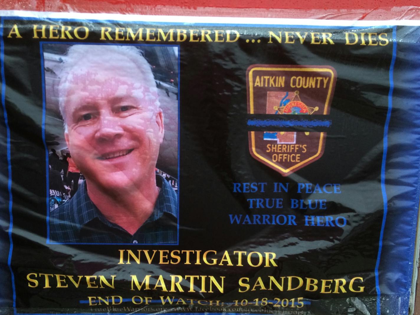 A rain-soaked sign honors fallen deputy Sandberg on a store in Aitkin.