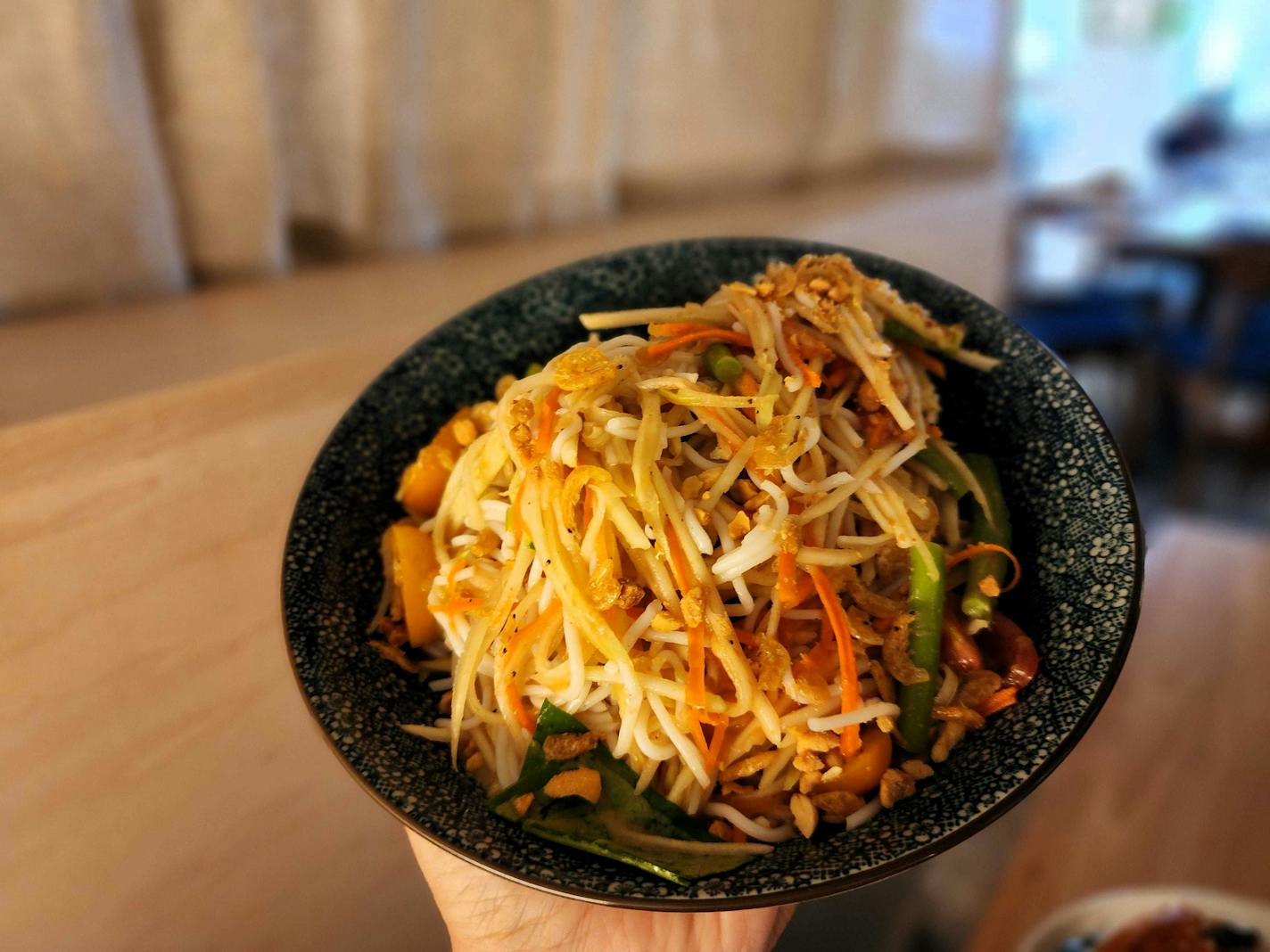 A black bowl containing threads of white noodles, orange carrots and green beans