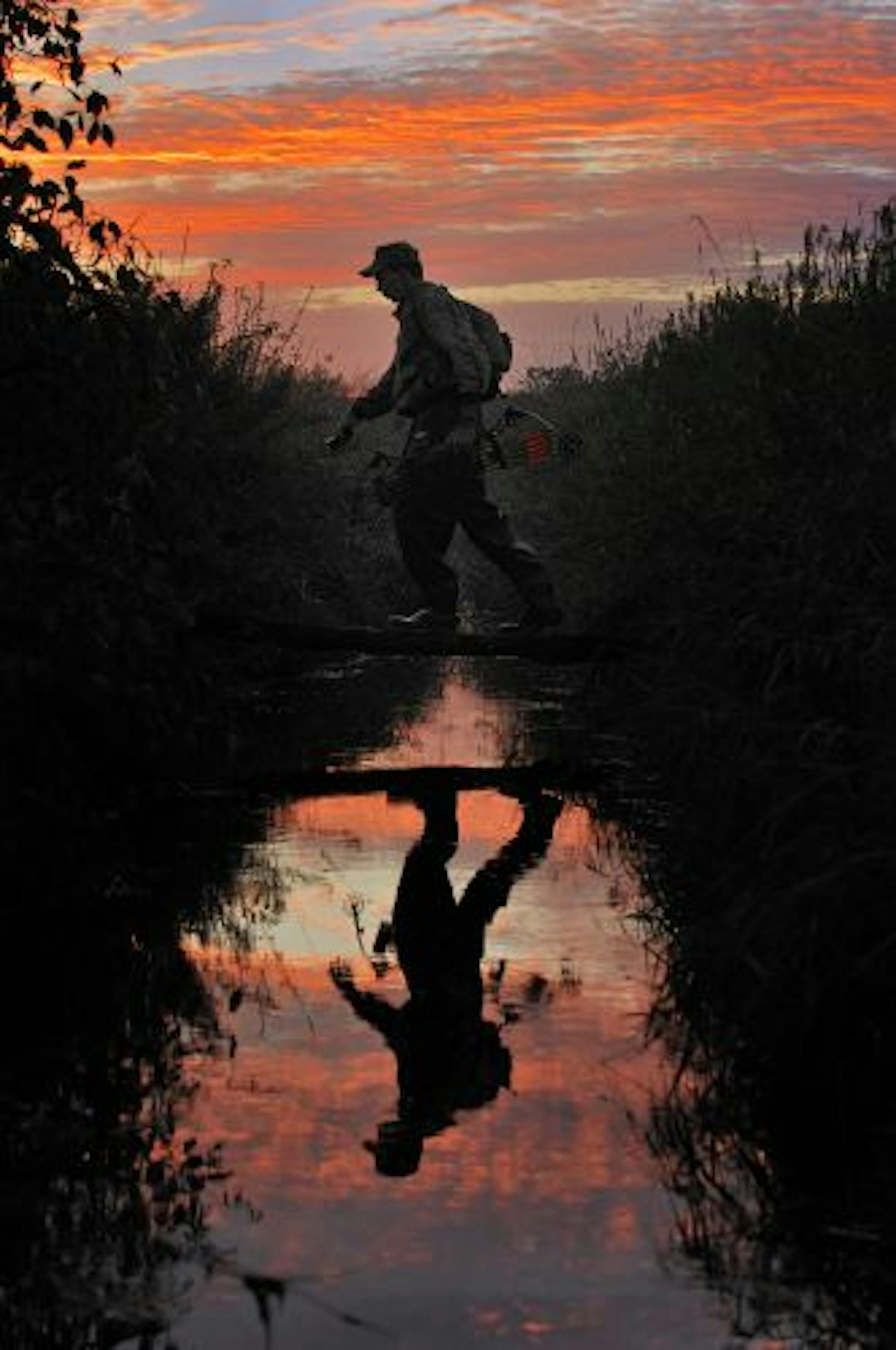 A hunter armed with bow and arrow crossed a log bridge over a creek. The deer hunting by archery and ruffed grouse seasons both opened Saturday.