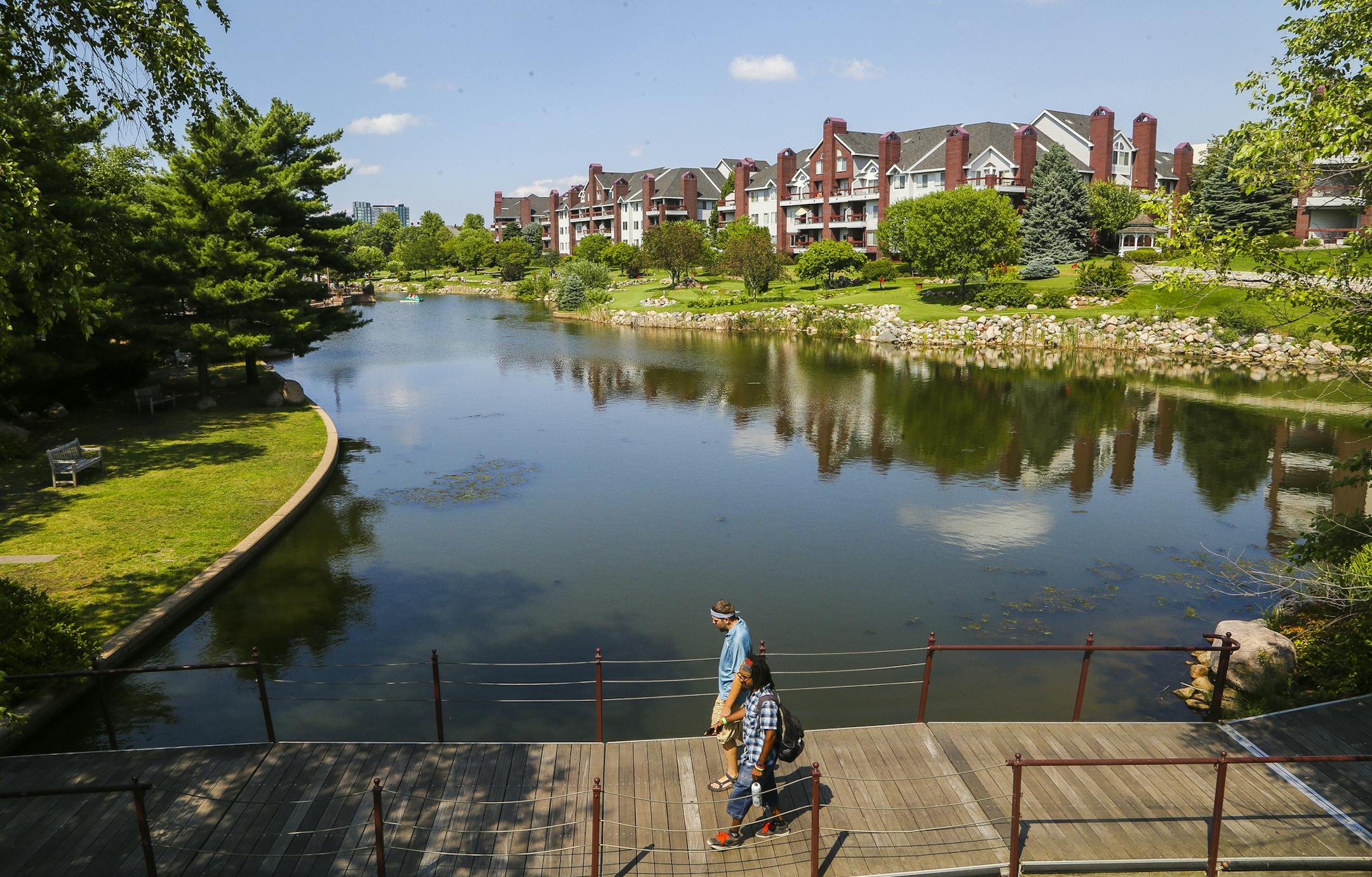 Avery Rowell, far bottom, and Rob Hoagberg, above, converse while walking over a brigge connectnig the park over the man-made pond. ] Timothy Nwachukwu &#x2022; timothy.nwachukwu@startribune.com Visitors enjoy a warm Minnesota summer afternoon at Centennial Lakes Park on Wednesday, July 20, 2016 in Edina. The development was recognized as one the the Great Places of 2014 by the Sensible Land Use Coalition.