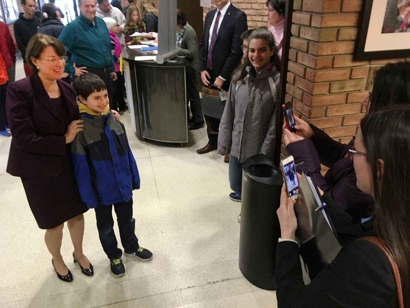 Jennifer Bagdade, far right, takes a photo of her son, Alex, standing with U.S. Senator Amy Klobuchar at the St. Paul Jewish Community Center on Sunday, March 19, 2017.