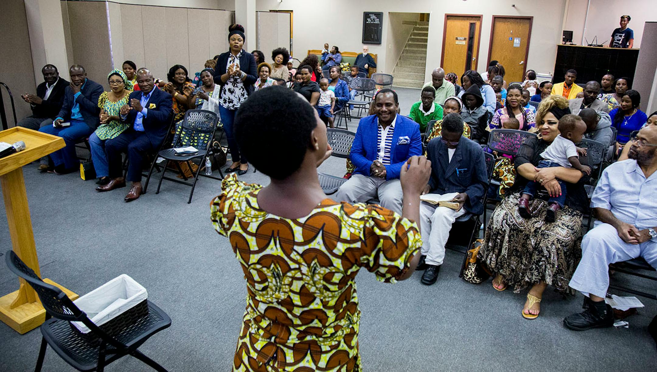 Members of the church service for African refugees watch as Elizabeth Nyerasaba sings, on Sunday evening.