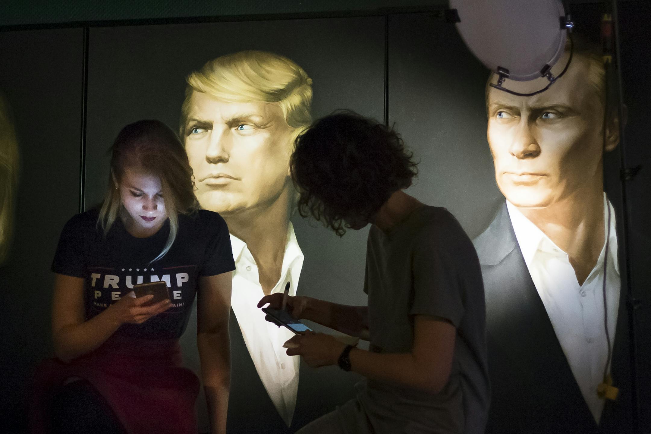 In this photo taken on Wednesday, Nov. 9, 2016, Maria Katasonova, left, looks at her smart phone during a live telecast of the U.S. presidential election in the Union Jack pub, with pictures of Donald Trump and Russian President Vladimir Putin in the back, in Moscow, Russia. Maria Katasonova, a pro-Kremlin political activist, said many Russians shuddered at the prospect of a Clinton victory because they hold her responsible for the breakdown in ties as secretary of state in Obama's first term. (