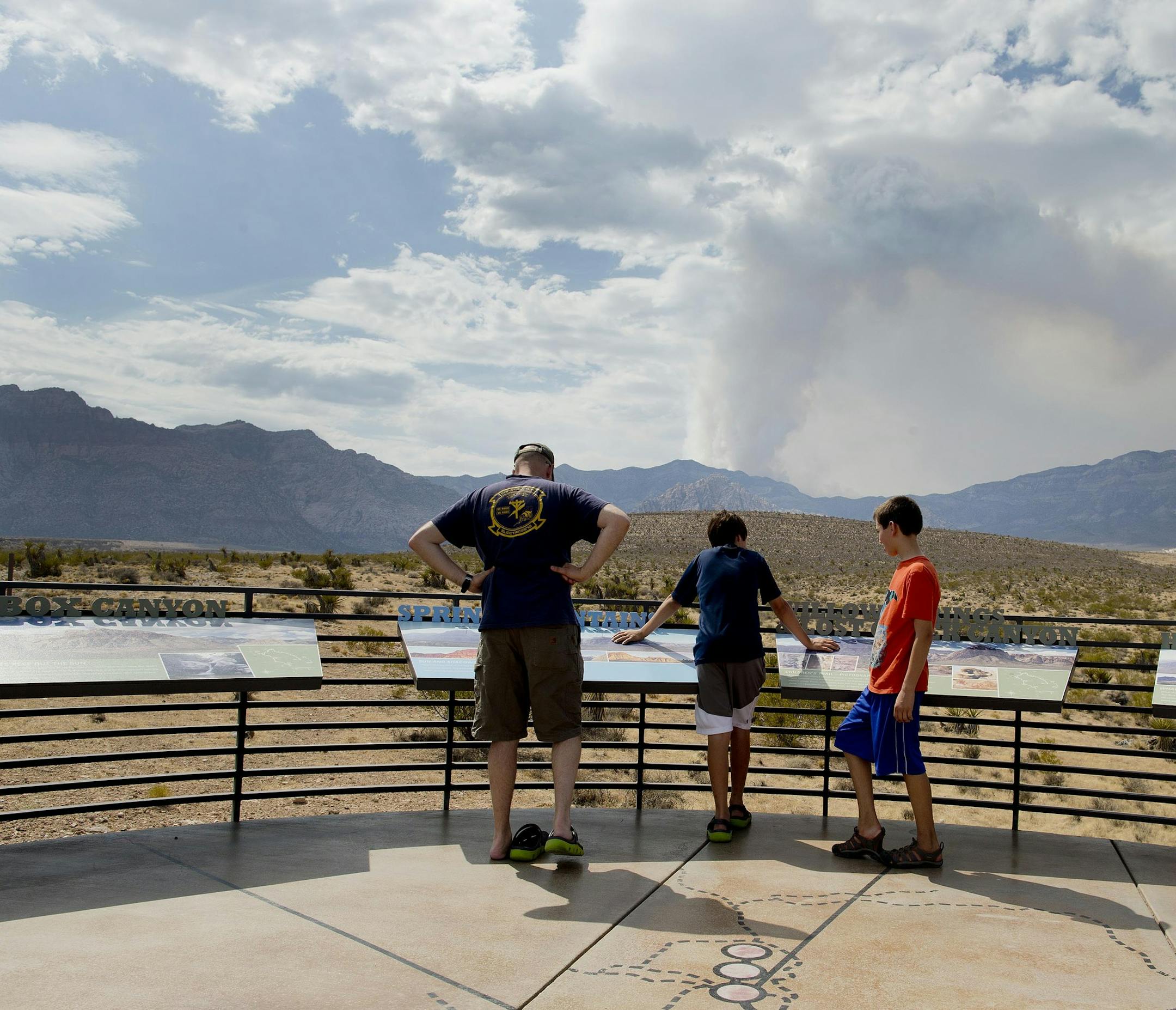 Visitors at Red Rocks National Recreation Area look out at the Spring Mountains with smoke billowing beyond from a wildfire on Mt. Charleston, Wednesday, July 10, 2013, near Las Vegas. More than 270 additional firefighters arrived Tuesday to help battle the fire sparked by lightning July 1, bringing to 1,077 the number of people fighting the blaze about 25 miles northwest of downtown Las Vegas. Overall containment dropped from 15 percent to 10 percent as erratic gusts of wind pushed flames up ca