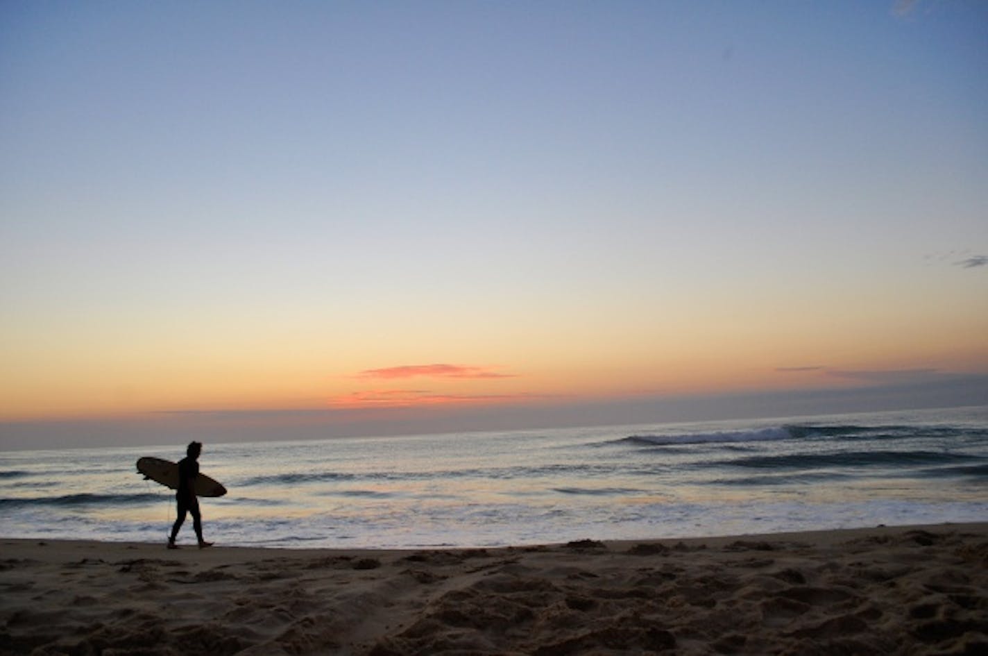 A surfer heading out before sunrise